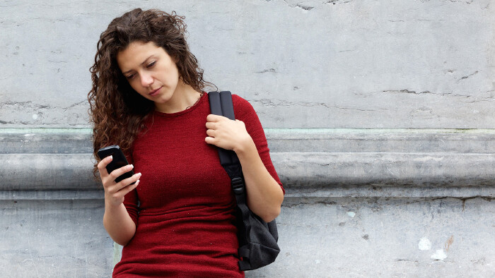 © mimagephotos, stock.adobe.com Junge Frau schaut mit ernstem Gesichtsausdruck auf ihr Smartphone